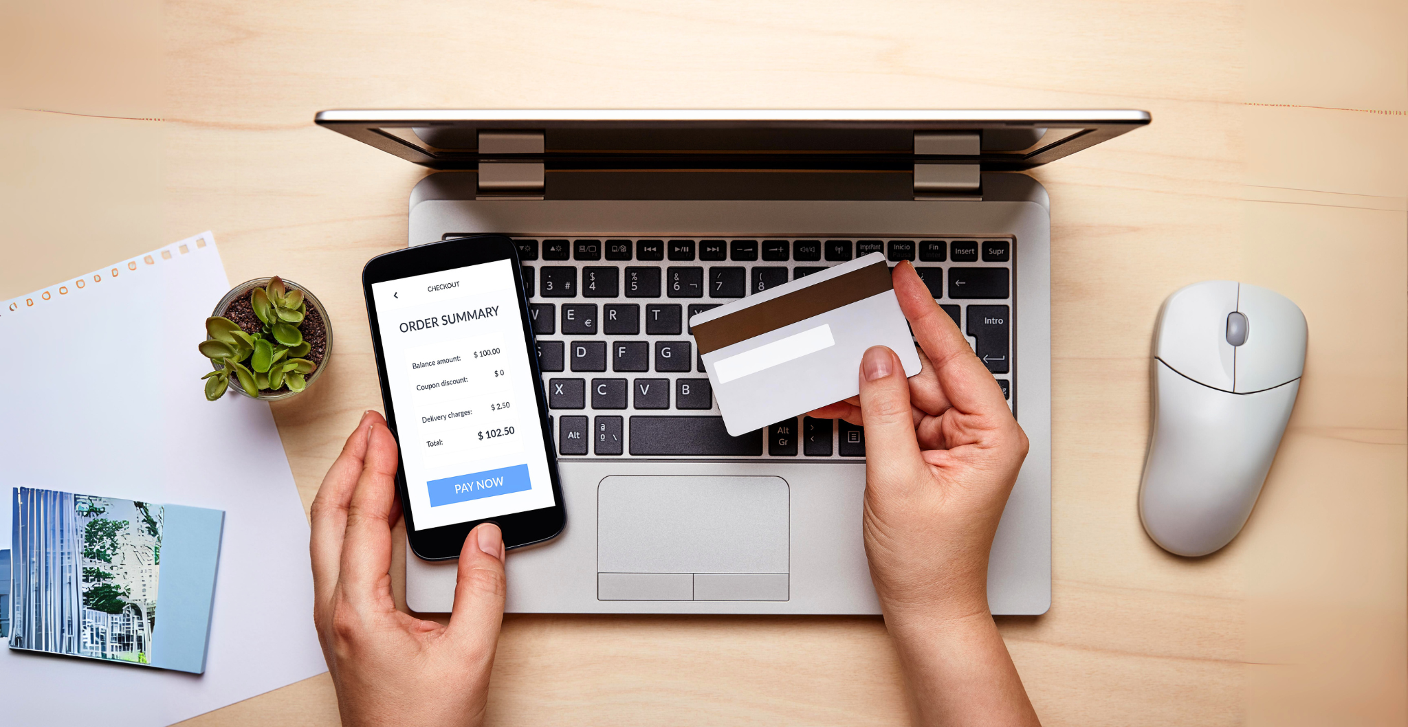 Hands holding a phone and bank card over a laptop, showing a digital payment in progress.